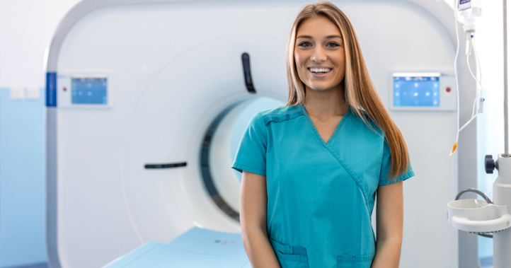A nurse in turquoise scrubs stands in front of a large medical scanning machine.